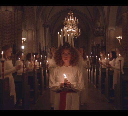 Lucia med tärnor lyser upp mörkret i kyrkan med sina ljus